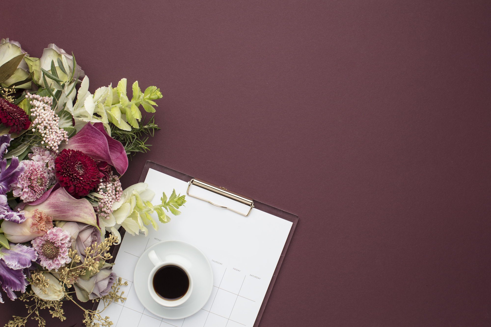 coffee cup and clipboard on a maroon background with a bouquet of flowers