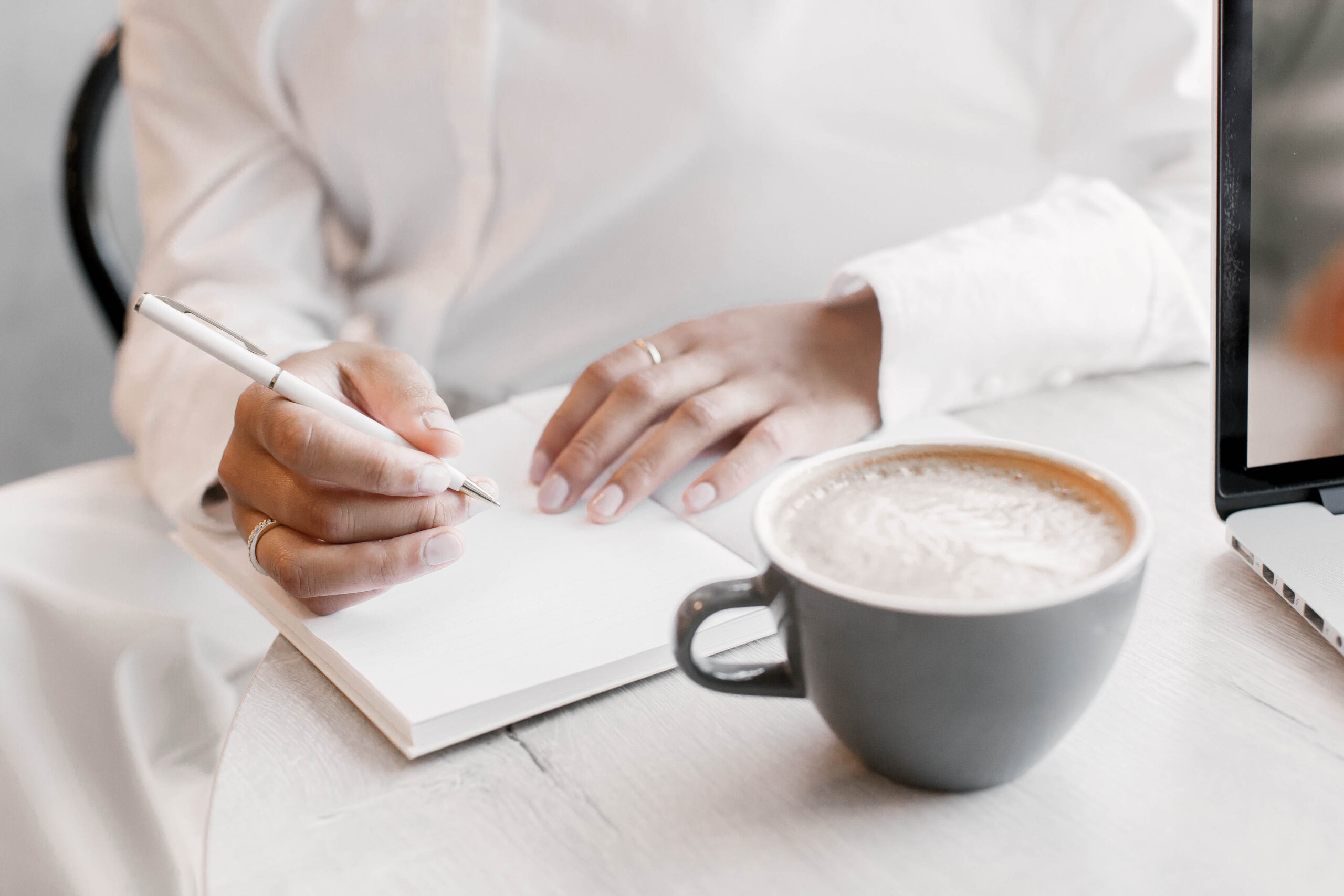 Woman writing in notebook with coffee cup on table